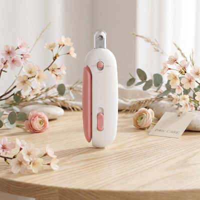 Coupe-griffes pour chat blanc et rose posé debout sur une table en bois clair, entouré de fleurs roses et de feuillage