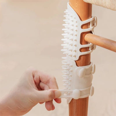 Mains fixant une brosse à chat blanche à picots autour d'un pied de meuble en bois grâce à ses sangles