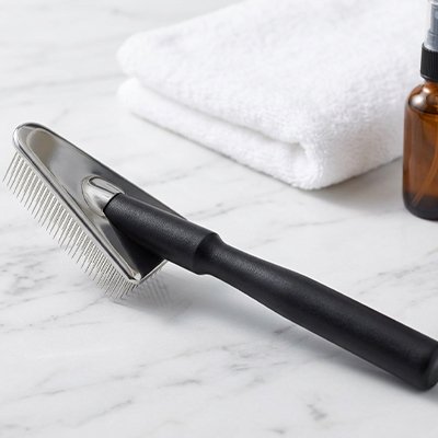 Brosse pour chat à poils longs avec manche noir et dents métalliques fines, posée sur un marbre blanc