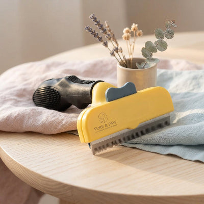Brosse jaune pour chat à poil court, avec manche noir et dents métalliques, posée sur une table en bois
