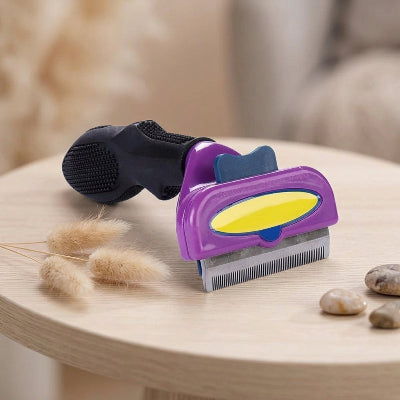Brosse violette pour chat à poil court, avec manche noir et dents métalliques, posée sur une table en bois clair à côté de touffes de poils