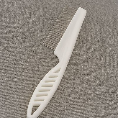 Peigne pour chat à manche blanc ajouré et à dents métalliques fines, posé sur un tissu gris